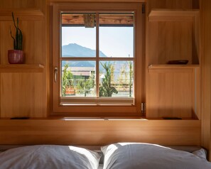 Een kamer met een bed, een raam met uitzicht op groen en bergen, houten wanden en een potplant.