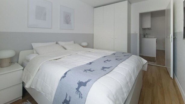 Quarto com cama, mesas de cabeceira, guarda-roupa e banheiro visível por uma porta aberta.