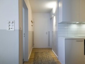 Ein schmaler Flur mit Holzboden führt zu einer Küchenzeile mit weißen Schränken und einem Einbauofen.