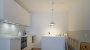 Uma cozinha moderna com armários brancos, forno embutido e uma pequena ilha com luminária pendente.