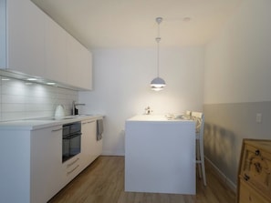 Eine moderne Küche mit weißen Schränken, einem eingebauten Ofen und einer kleinen Kochinsel mit Pendelleuchte.