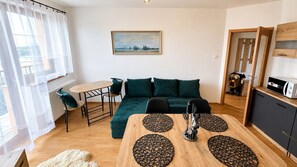 A modern living room with a sofa, a dining table with placemats, a kitchen area with a microwave, and a painting on the wall. - 2 room Apartment, mountains view, Stará Lesná (Stará Lesná)