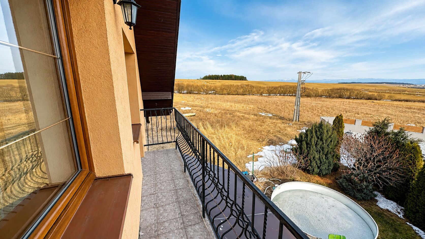 Un balcon donnant sur un paysage rural, avec une rambarde en métal et une antenne parabolique.