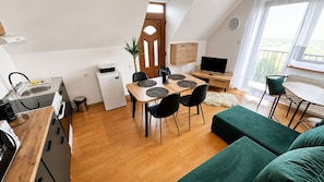 Una cocina compacta con electrodomésticos modernos, un comedor con una mesa de madera y sillas negras, y un sofá verde en una habitación luminosa con vistas.