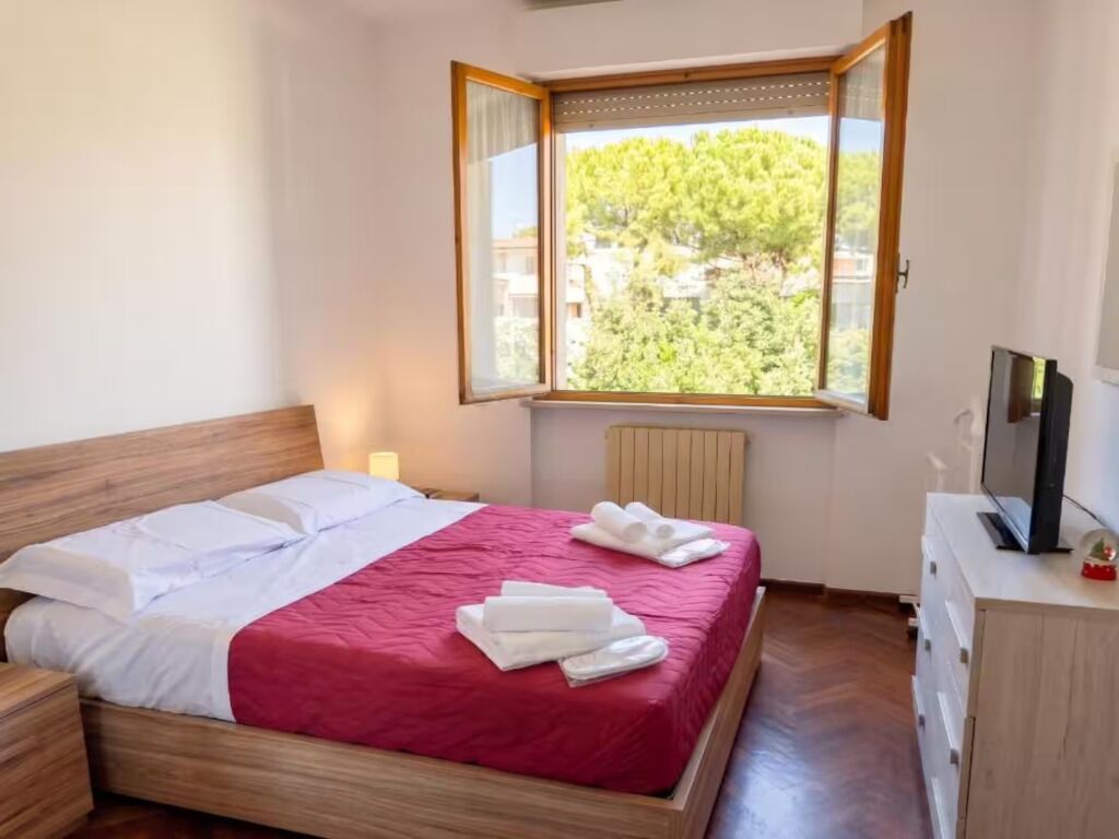 Een slaapkamer met een bed, een televisie en een raam met uitzicht op bomen.