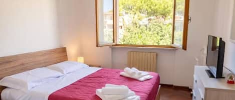 Une chambre à coucher avec un lit, une télévision et une fenêtre donnant sur des arbres.