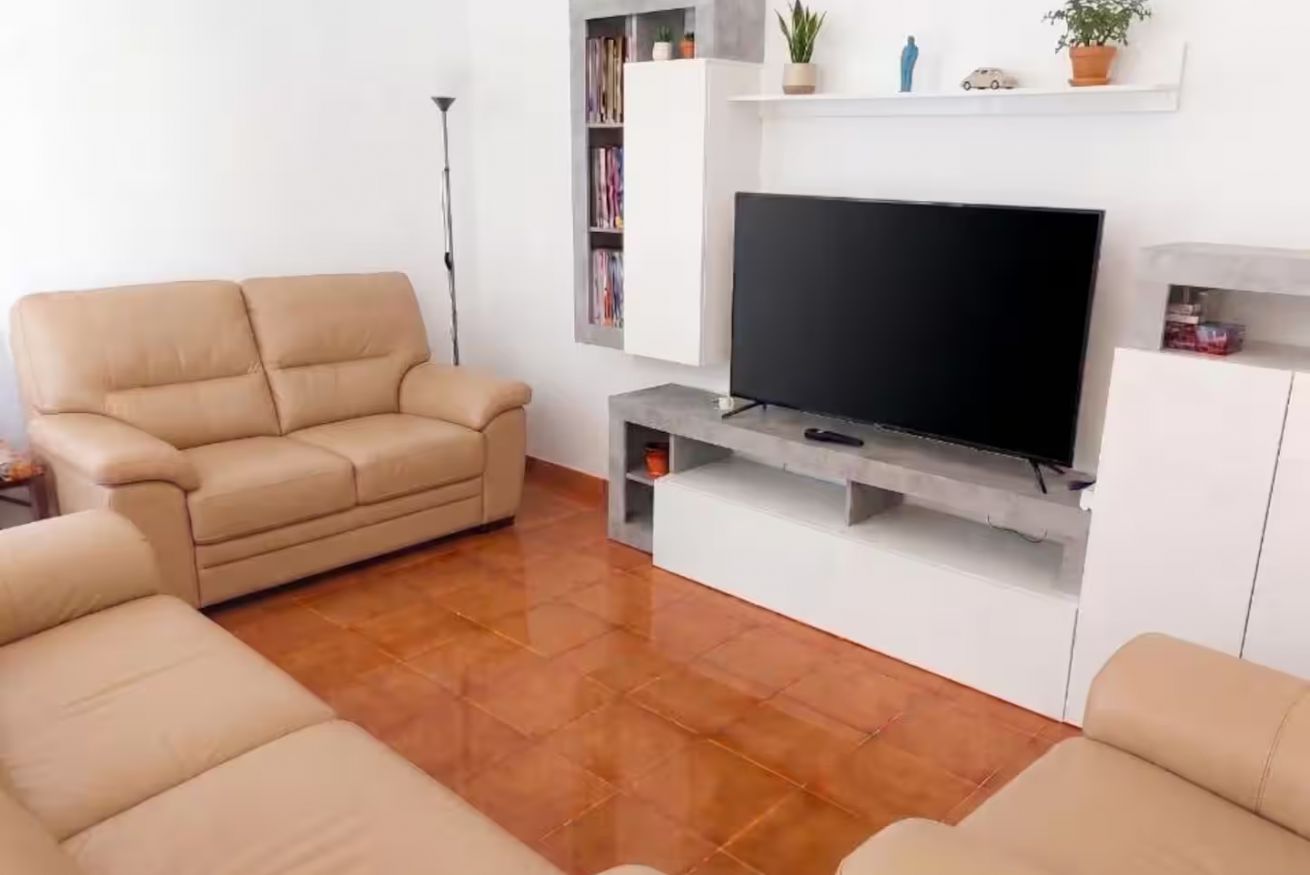 Ein Wohnzimmer mit einer Couch, einem Flachbildfernseher, einem Bücherregal und einer Stehlampe.