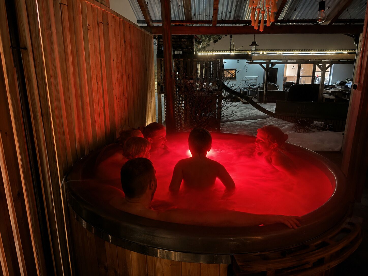Ett bubbelbad med folk i, omgivet av träväggar och ett tak av metall.