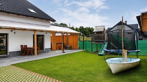 A backyard with a covered patio, a trampoline, and a boat.