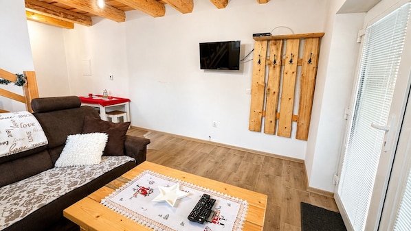 A cozy living room with a brown sofa, a wooden coffee table with a star decoration, a television mounted on the wall, and a wooden rack with hooks.