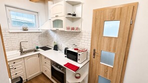 A compact kitchen with a sink, stove, microwave, and white cabinetry. - Apartment house, sauna and jacuzzi, Svätý Kríž 1 (Svätý Kríž)