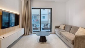 Uma sala de estar moderna com televisão de tela plana, mesa de centro redonda, sofá e porta de vidro deslizante que dá para uma área externa.