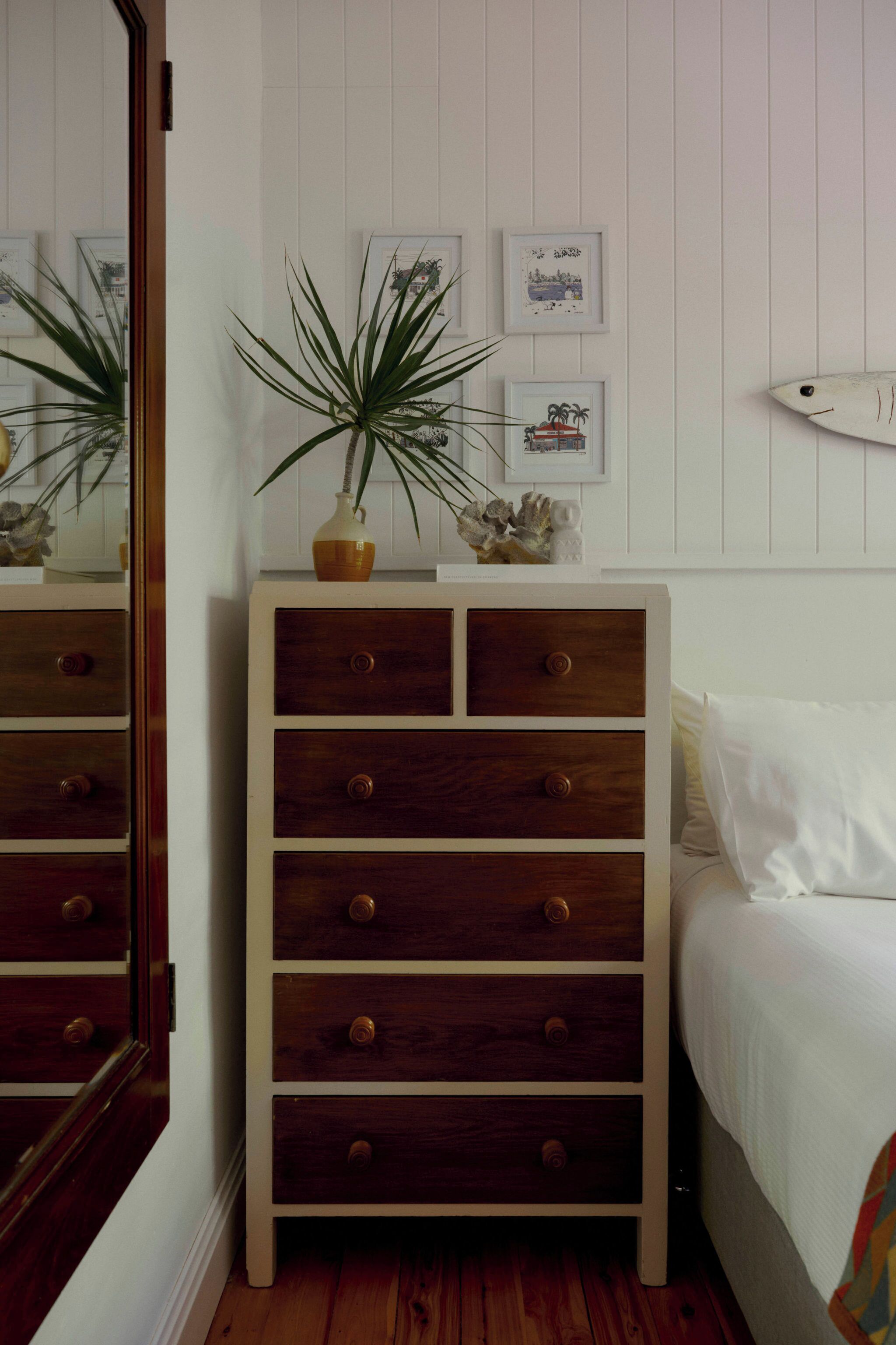 A bedroom with a wooden dresser, a bed, and a wall with framed pictures.