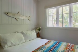 A bedroom with a bed, pillows, a wall-mounted fish decoration, a window with a view of greenery, and a bedside plant. - Bruns Surf Shack: Beachy Hideaway. Pet friendly! (Brunswick Heads)
