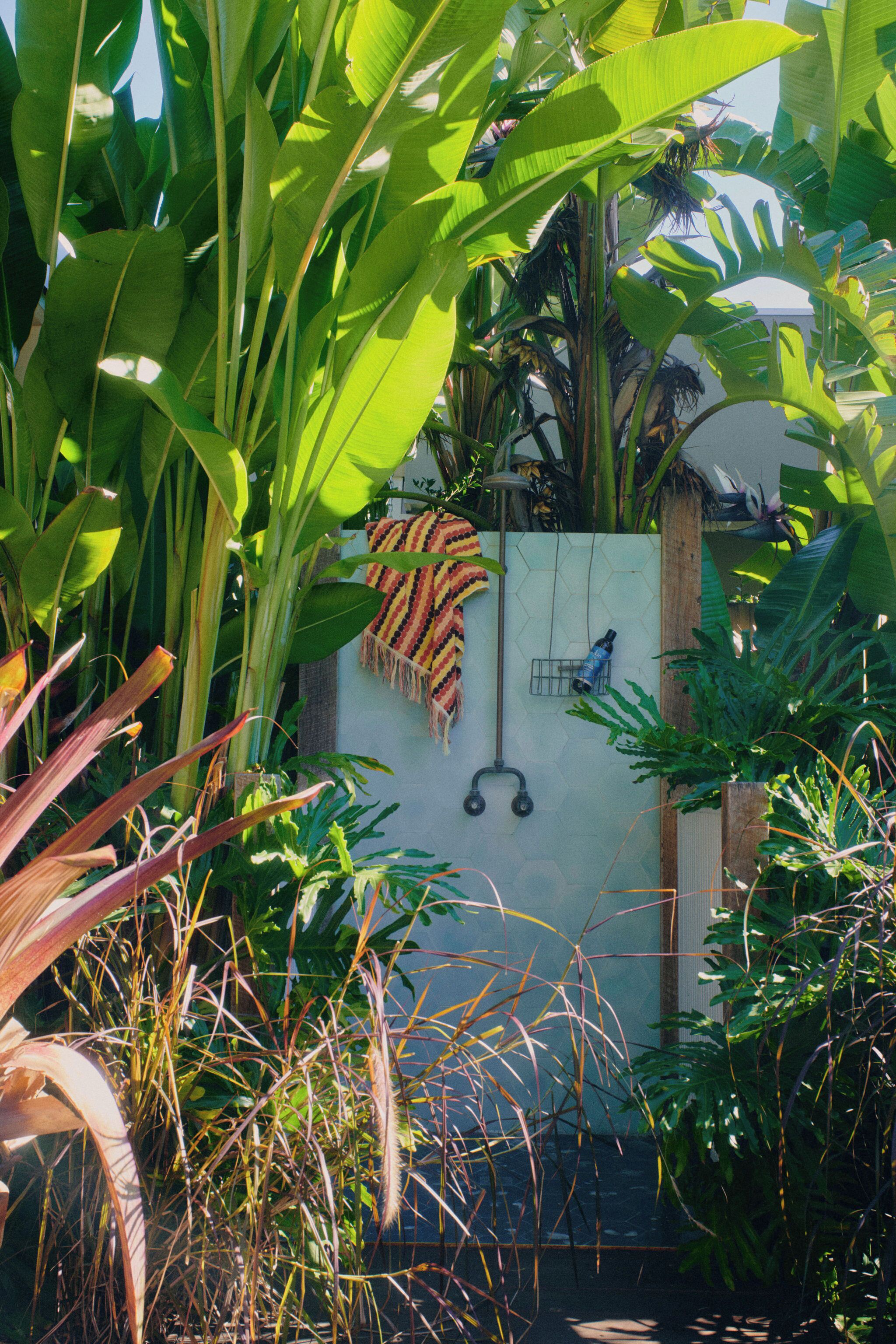 A lush garden with banana trees, a hammock, and a shower area with a tiled wall.