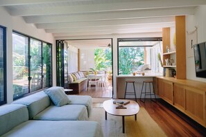 A modern living room with a sofa, a coffee table, and a kitchen area with a bar and stools. - Bruns Surf Shack: Beachy Hideaway. Pet friendly! (Brunswick Heads)