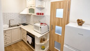 Eine kompakte Küche mit Mikrowelle, Toaster und Kühlschrank. Es gibt Schränke mit Glastür, ein Spülbecken und eine Holztür mit kleinem Fenster.