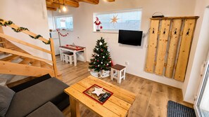 A cozy room with a wooden staircase, a small dining area, a Christmas tree, and a television mounted on the wall.