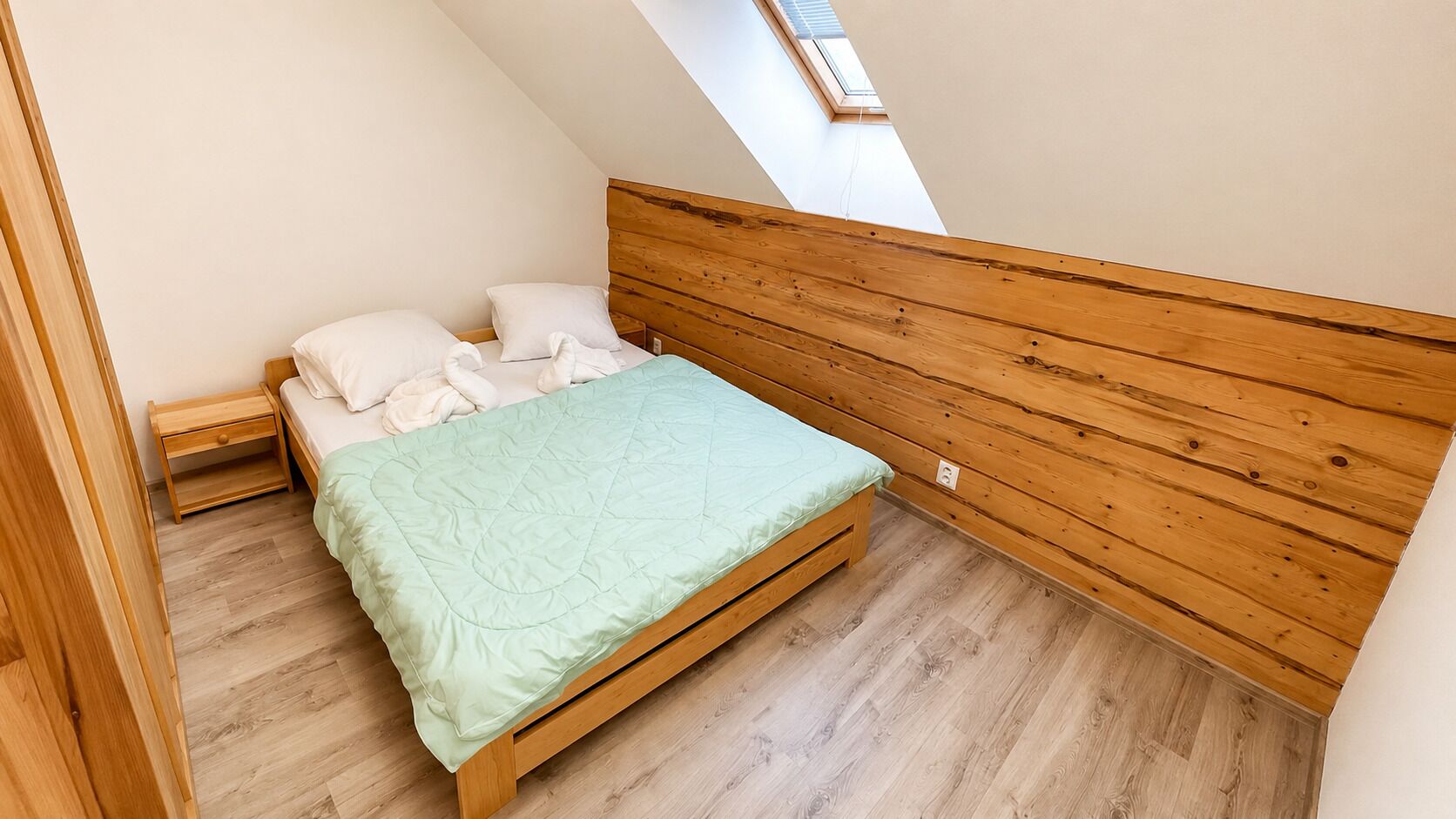 A small, single-bed room with a sloped ceiling and wooden headboard.