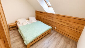 A small, single-bed room with a sloped ceiling and wooden headboard.