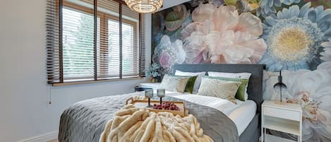 A bedroom with a large bed, a decorative wall mural, a hanging light fixture, and a bedside table.