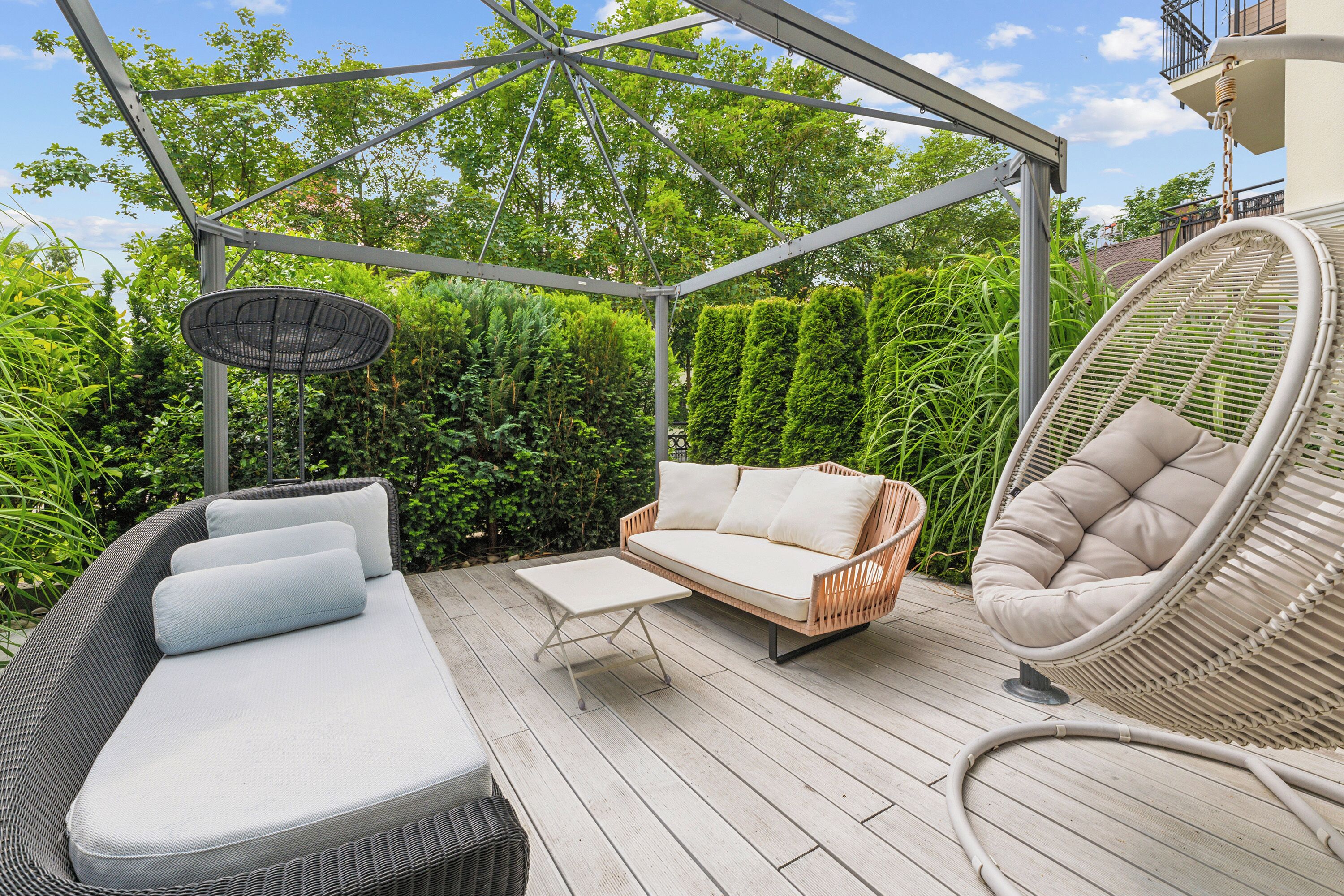 An outdoor patio with a covered seating area, a dining table, and a hanging chair.