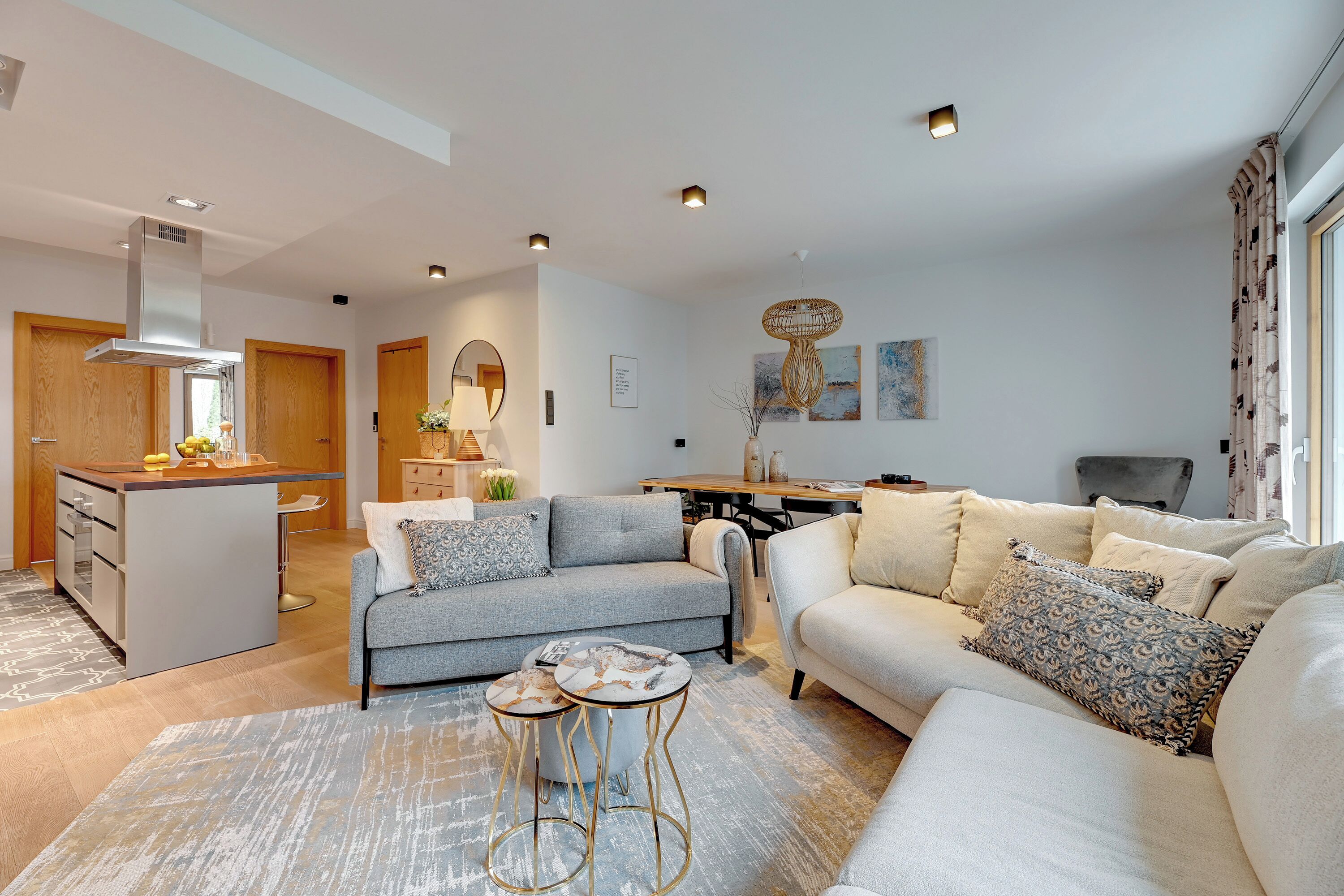 A modern living room with a grey sofa, a beige sofa, and a coffee table. There is a kitchen area with a stove and a sink.