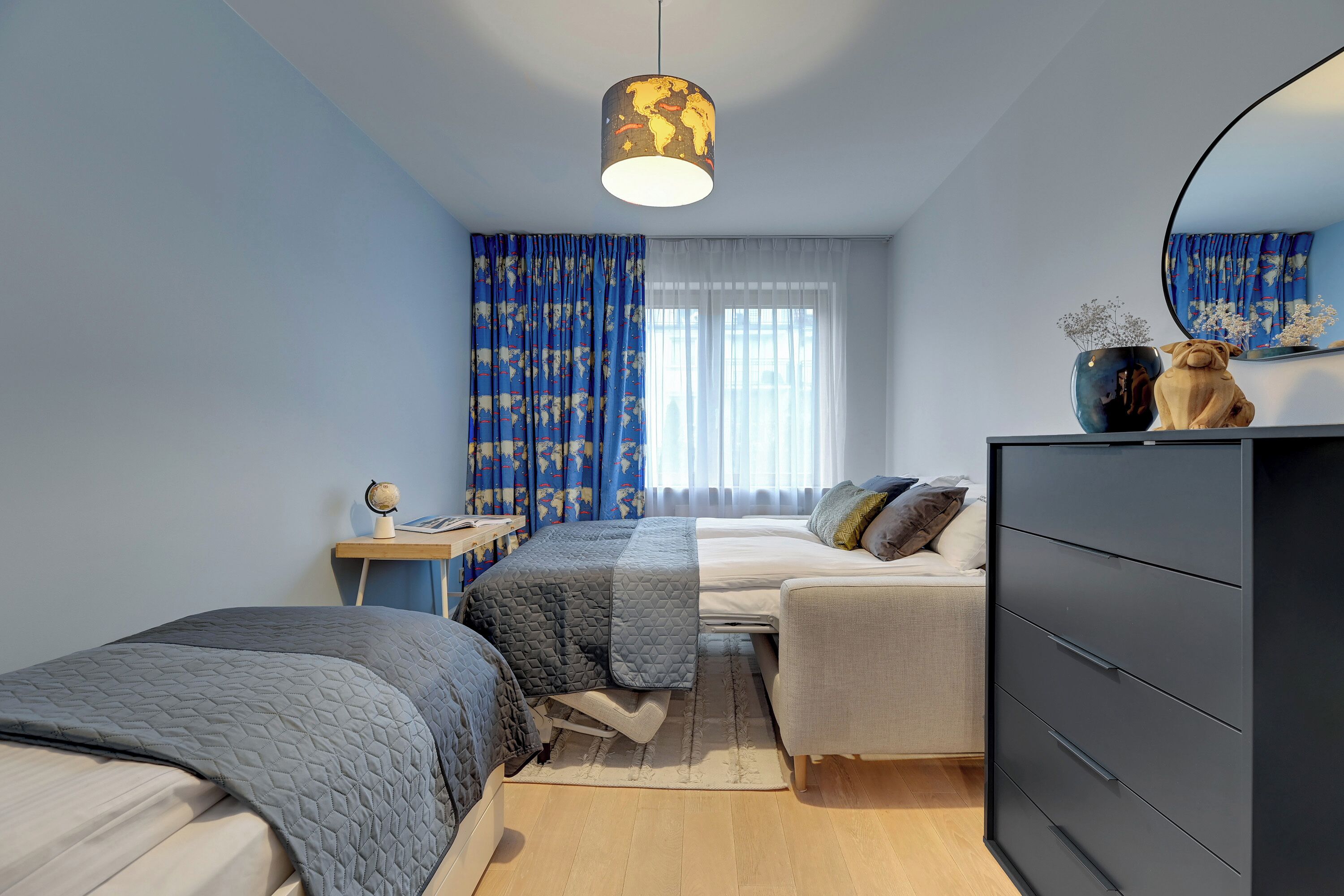 Une chambre avec deux lits, une commode, un globe terrestre posé sur une table de chevet et une fenêtre avec des rideaux.