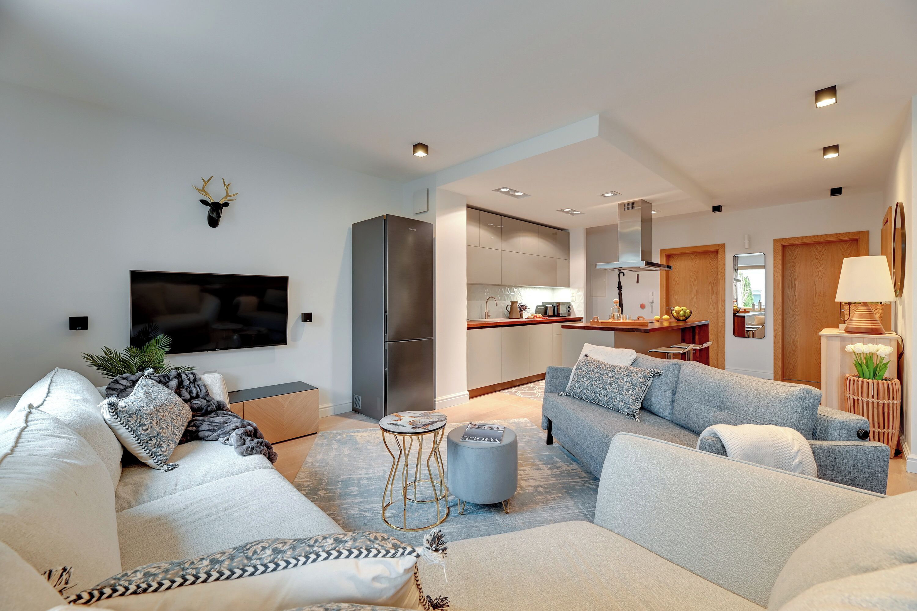 A modern living room with a sofa, a television, and a kitchen in the background.
