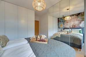 A modern bedroom with a large bed, a wooden bedside table with glasses and grapes, a mirror, and a floral wall mural. - TULUM Jelitkowo with Terrace and Parking (Gdańsk)