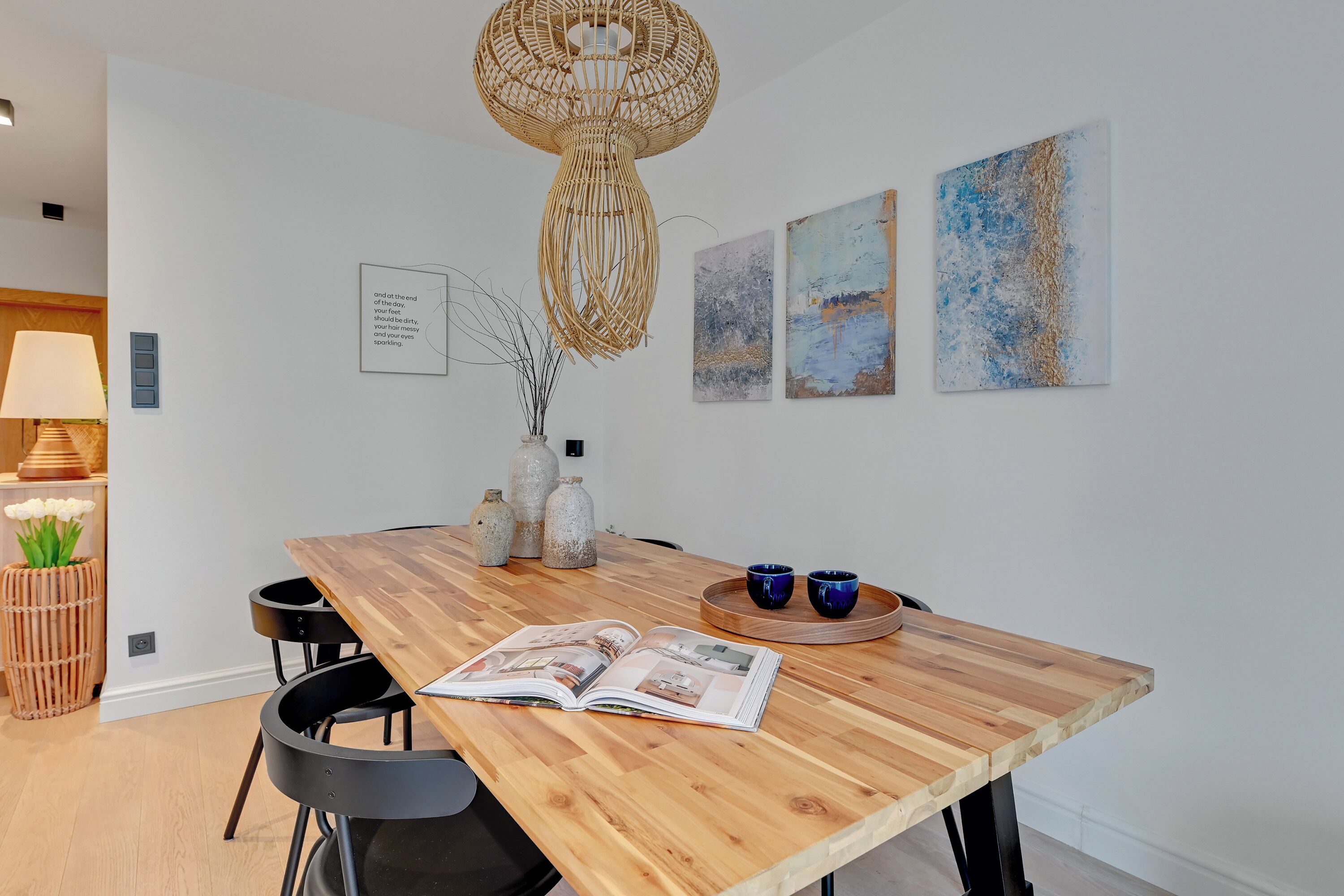 A dining area with a wooden table, chairs, a hanging light fixture, and wall art.
