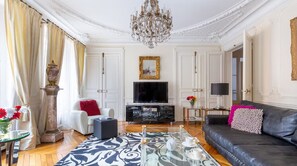 Una habitación con candelabro, televisor, sofá y alfombra estampada.