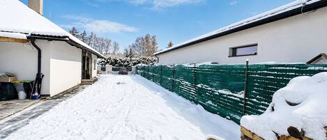A snow-covered pathway leading to a building with a green fence and a chimney.