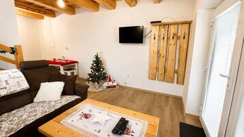 A cozy living room with a brown sofa, a wooden coffee table, a small Christmas tree, and a mounted television.