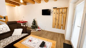 A cozy living room with a brown sofa, a wooden coffee table, a small Christmas tree, and a mounted television.