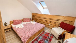 A bedroom with a sloped ceiling, a wooden headboard, a bed with patterned bedding, a red chair, a small table, and a window. - Apartment house, sauna and jacuzzi, Svätý Kríž 3 (Svätý Kr íž)