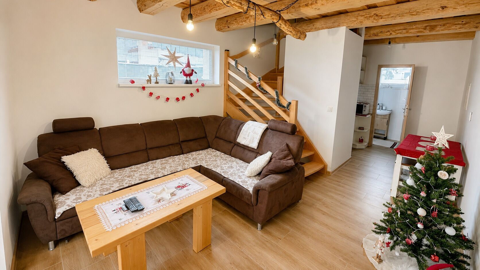Una sala de estar acogedora con un sofá seccional marrón, una mesa de centro de madera y una escalera que lleva a un nivel superior.