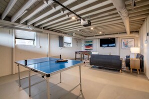 Une pièce équipée d’une table de ping-pong, d’un canapé, d’un téléviseur et d’un projecteur fixé au plafond.