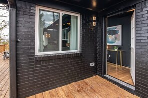A black brick exterior with a wooden deck and a glass door leading inside.