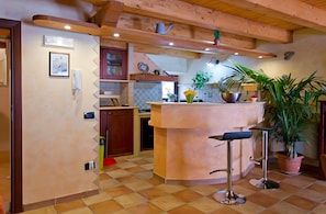 A kitchen with a central island, wooden beams, tiled flooring, and various kitchen appliances.