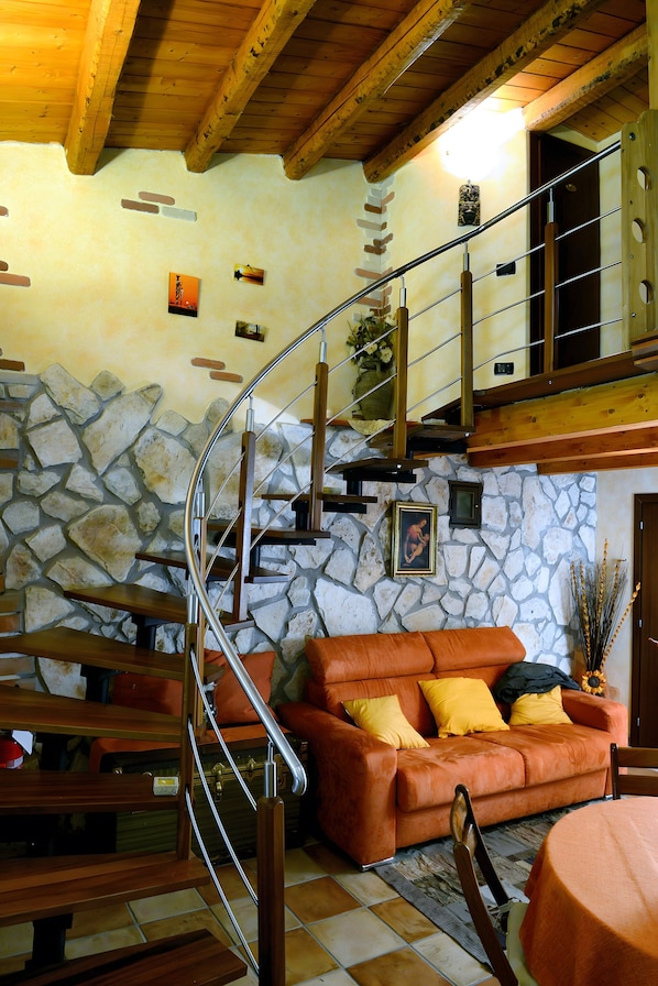 A wooden staircase with a stone wall backdrop, a leather sofa with cushions, and a wooden bench.