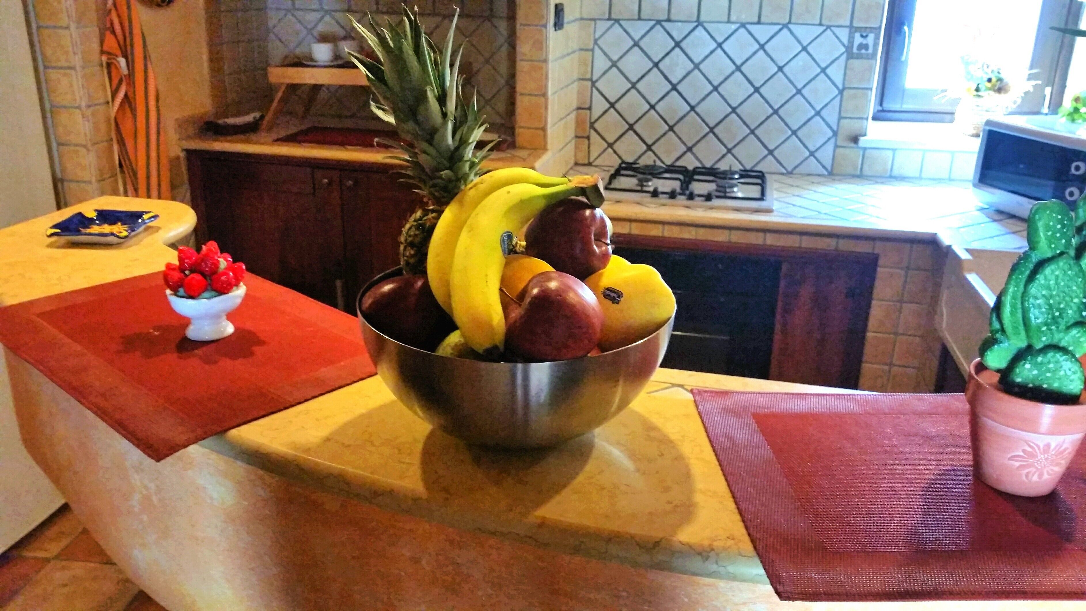 A kitchen counter with a fruit bowl containing bananas, apples, and a pineapple.