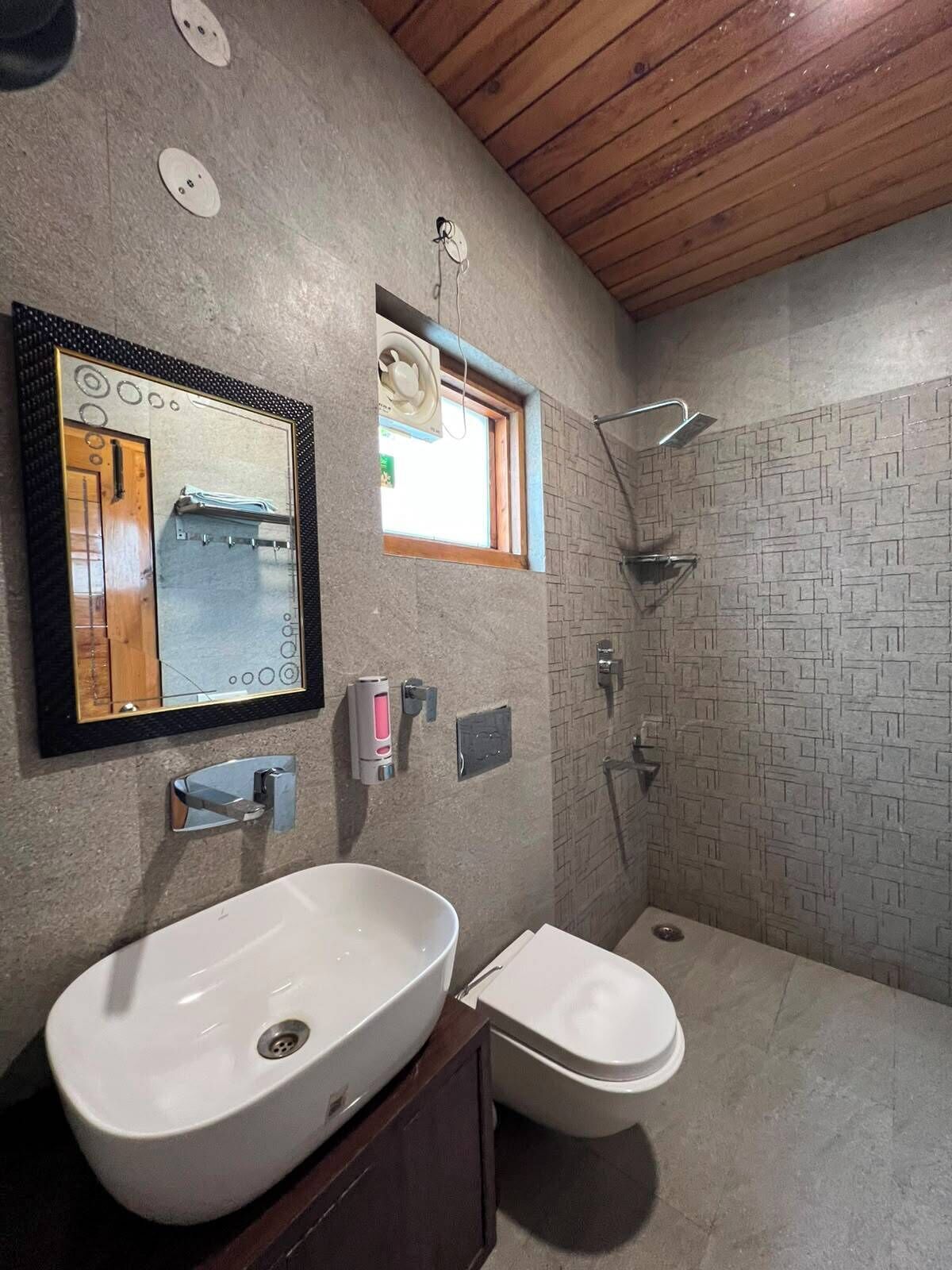 Een badkamer met een grote spiegel, een wastafel, toilet, douche en een raam.