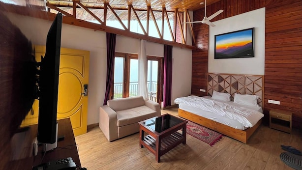 A room with a bed, a sofa, a television, and a painting on the wall.