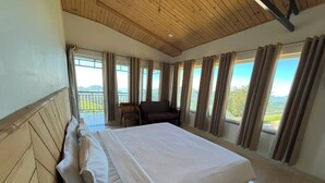 A bedroom with a large bed, wooden headboard, and multiple windows with curtains.