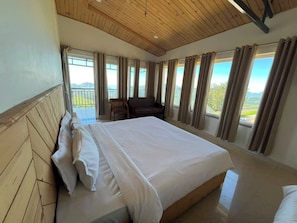 A bedroom with a large bed, wooden headboard, and multiple windows with curtains.
