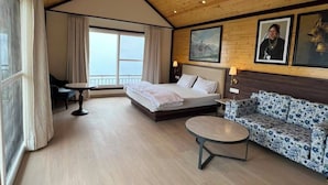 A spacious room with a bed, a sofa, a round table, and a ceiling fan.