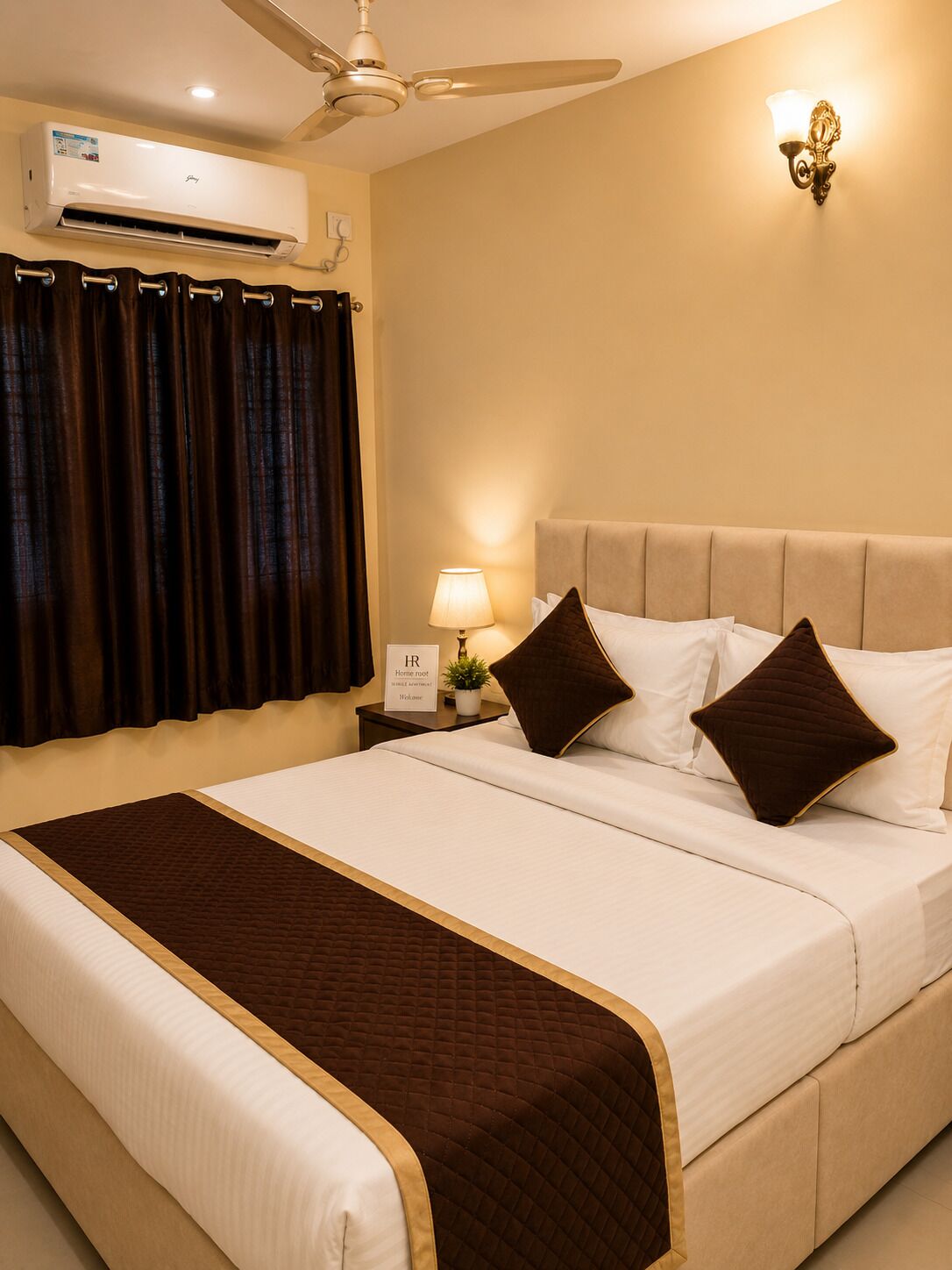 Habitación de hotel con cama, mesita de noche, lámpara, luz en la pared y ventilador de techo, además de un equipo de aire acondicionado.