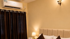 Quarto de hotel com cama, mesa de cabeceira, luminária, iluminação embutida na parede, ar condicionado e ventilador de teto.
