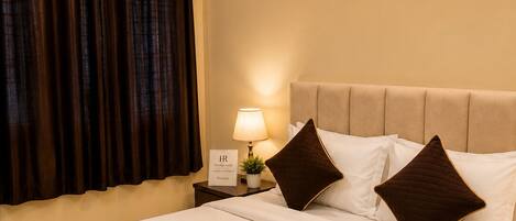 Habitación de hotel con cama, mesita de noche, lámpara, luz en la pared y ventilador de techo, además de un equipo de aire acondicionado.